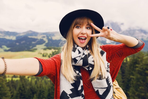 Jeune femme joyeuse souriant, prenant selfie et montrant des mains de signes