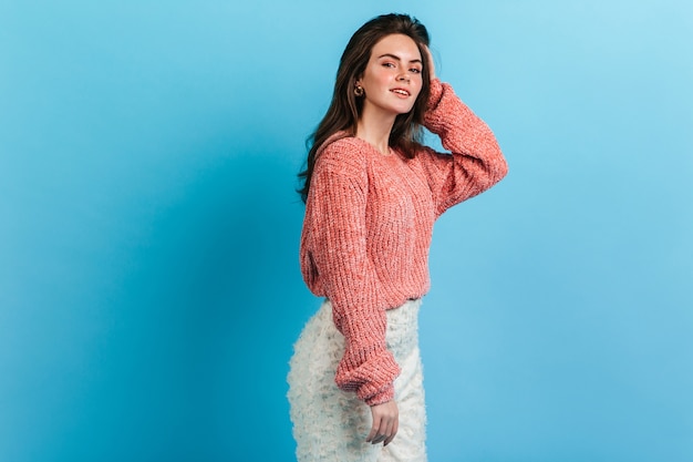 Jeune femme en jupe blanche élégante posant sur un mur bleu. Modèle avec des ombres à paupières roses souriant