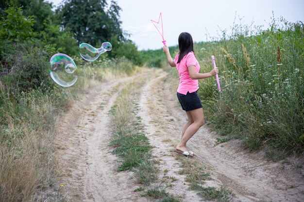 Une jeune femme lance d'énormes bulles de savon en arrière-plan belle nature, vue arrière.