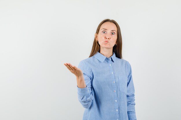 Jeune femme levant la main de manière interrogative en chemise bleue et à la colère.