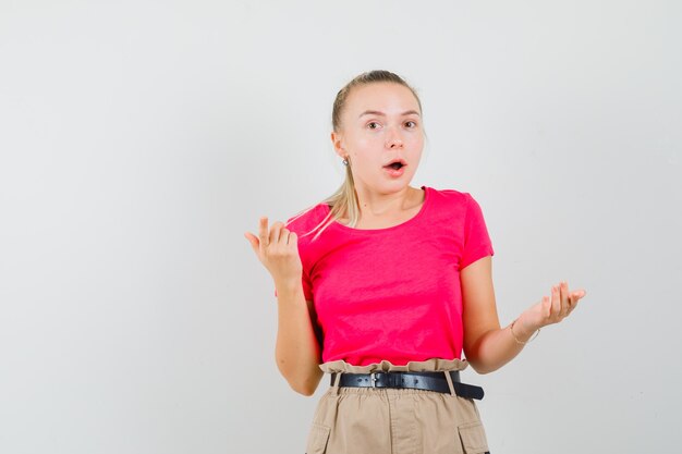 Jeune femme levant les mains en geste étonné en t-shirt et pantalon rose