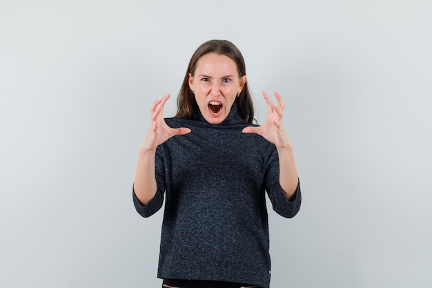 Jeune femme levant les mains de manière agressive en vue de face de chemise décontractée.