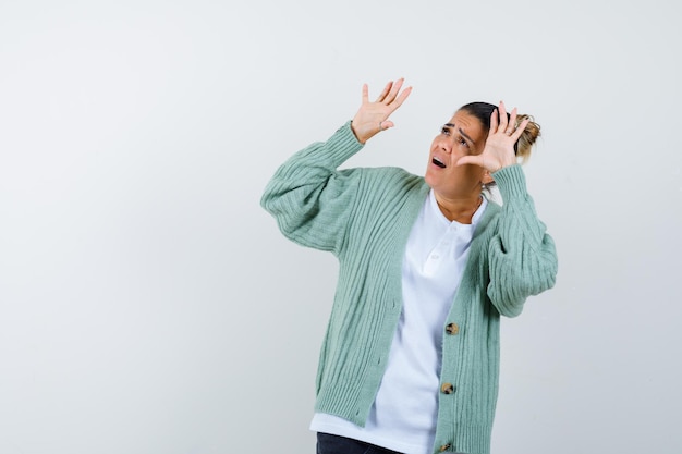 Jeune femme levant les mains et regardant au-dessus en t-shirt blanc et cardigan vert menthe et ayant l'air effrayé