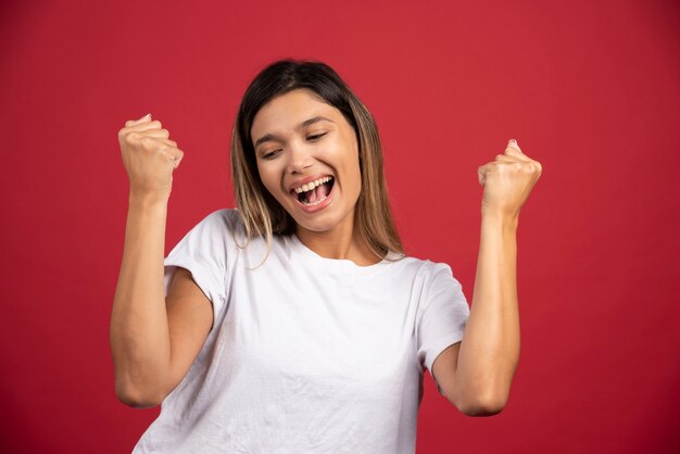 Jeune femme levant les poings sur le mur rouge.