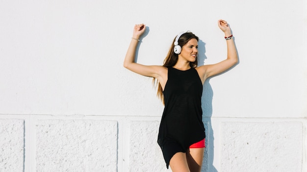 Photo gratuite jeune femme levant ses mains tout en écoutant de la musique sur un casque