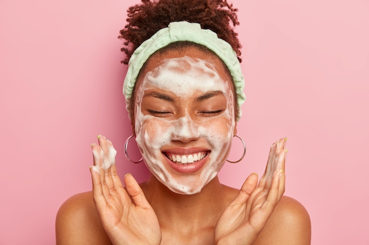 Photo gratuit jeune femme lève les paumes sur le visage, garde les yeux fermés, montre des dents blanches, utilise une mousse nettoyante pour les soins de la peau, obtient un vrai plaisir