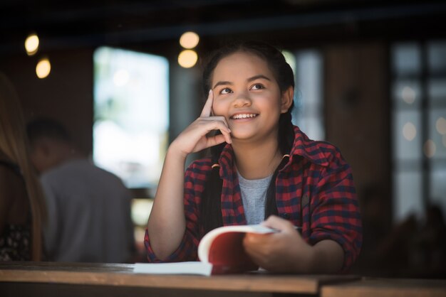 Jeune femme lisant livre assis pensant intérieur au café urbain.