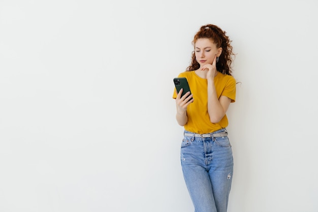 Jeune femme lisant un message sur un smartphone et souriant sur les réseaux sociaux en se tenant debout sur fond blanc