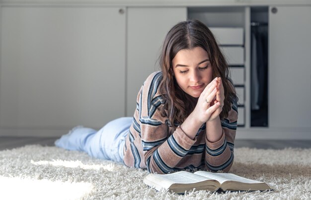 Une jeune femme lit la bible allongée sur le sol