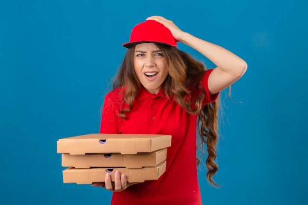 Photo gratuite jeune femme de livraison portant un polo rouge et une casquette debout avec des boîtes à pizza choqué avec la main sur la tête pour erreur se souvenir d'erreur oublié mauvais concept de mémoire sur fond blanc isolé