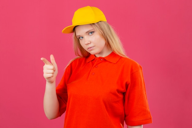 Photo gratuite jeune femme de livraison portant un polo rouge et une casquette jaune pointant l'index vers la caméra à la confiance sur fond rose isolé