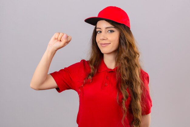 Jeune femme de livraison portant un polo rouge et une casquette en levant le poing après une victoire face heureux concept gagnant sur fond blanc isolé