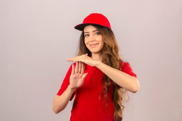 Jeune femme de livraison portant un polo rouge et une casquette souriant faisant le geste de temps sur fond blanc isolé