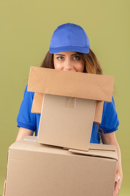 Photo gratuite jeune femme de livraison tendue avec look sournois portant un polo bleu et une casquette debout avec pile de colis sur fond vert isolé