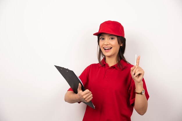 Jeune femme de livraison en uniforme rouge avec presse-papiers sur fond blanc.