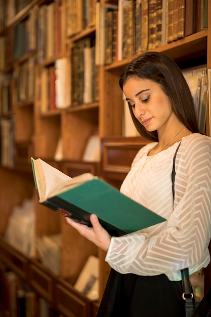 Photo gratuite jeune femme, livre lecture, près de, étagère