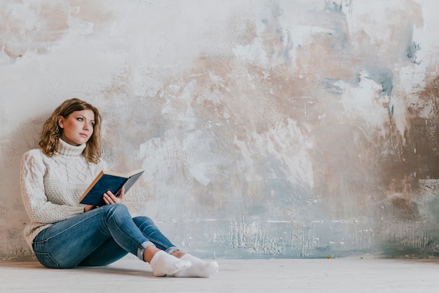 Jeune femme avec un livre près du mur