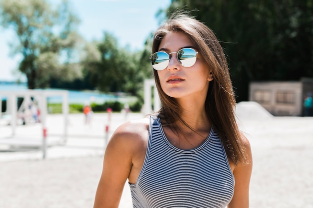 Jeune femme à lunettes de soleil debout sur la plage