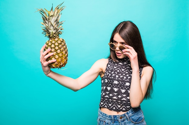 Jeune femme à lunettes de soleil vêtements décontractés withp avec ananas en mains isolés