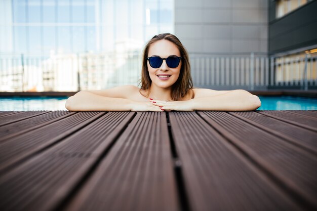 Jeune femme à lunettes avec un sourire blanc parfait se baignant dans une piscine en vacances