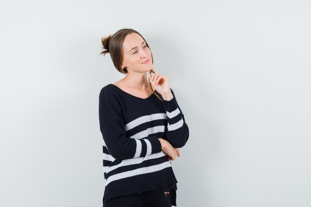 Jeune femme en maille rayée et pantalon noir debout dans la pensée pose et regardant à droite et à la recherche