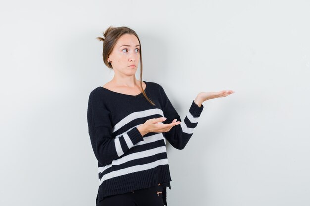 Jeune femme en maille rayée et pantalon noir s'étendant les mains comme tenant quelque chose d'imaginaire et à la sérieuse