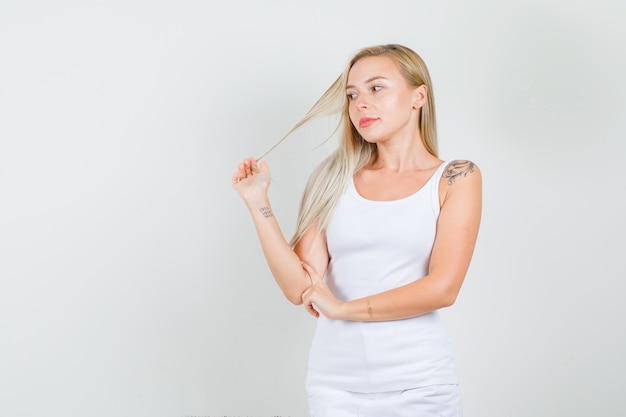 Photo gratuite jeune femme en maillot blanc, mini jupe posant tout en tenant le brin avec la main et à la mignon