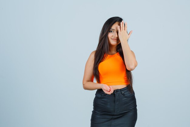 Jeune femme en maillot, mini jupe couvrant les yeux avec la main et à la charmante, vue de face.