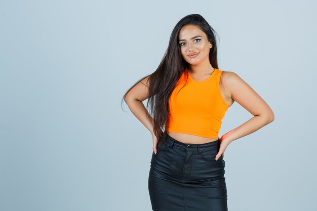 Jeune femme en maillot, mini jupe gardant les mains sur la taille et regardant glamour, vue de face.