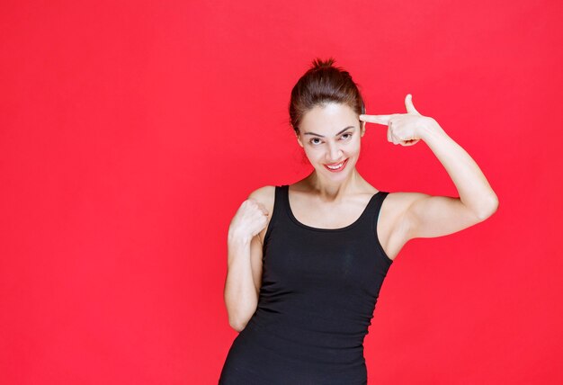 Jeune femme en maillot noir debout sur le mur rouge et pensant