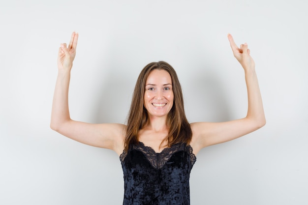 Photo gratuite jeune femme en maillot noir levant les bras avec deux doigts et à la joyeuse