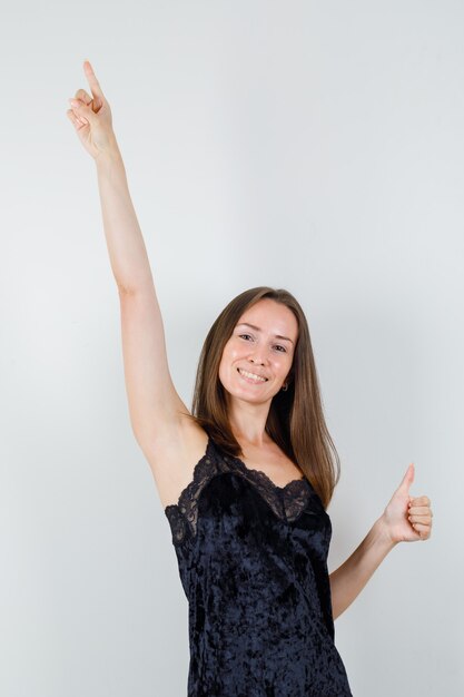 Jeune femme en maillot noir pointant vers le haut avec le pouce vers le haut et à la joyeuse