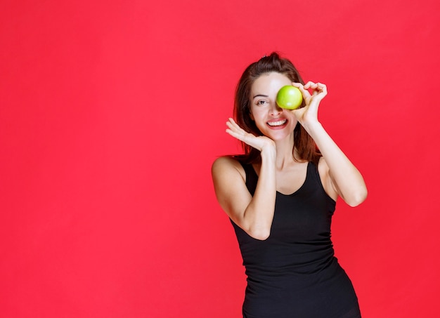 Jeune femme en maillot noir tenant des pommes vertes à ses yeux
