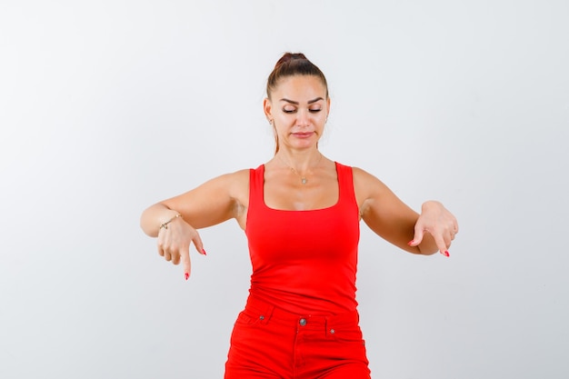 Jeune femme en maillot rouge, pantalon rouge pointant vers le bas et regardant attentivement, vue de face.