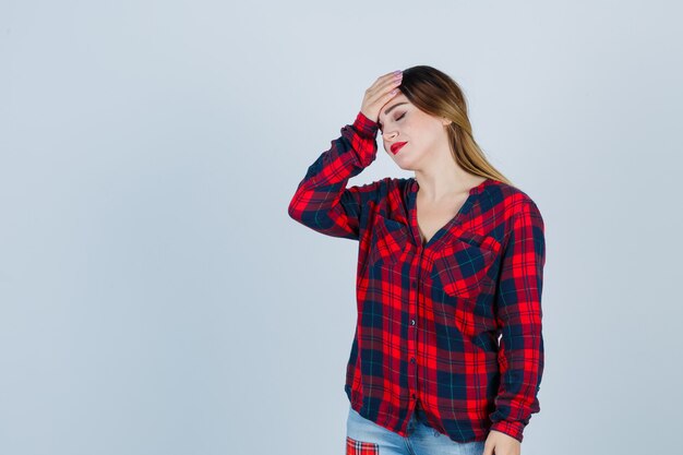 Jeune femme avec la main sur le front en chemise à carreaux et à l'oubli. vue de face.