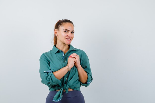 Jeune femme avec les mains jointes sur la poitrine en chemise verte et l'air joyeux, vue de face.