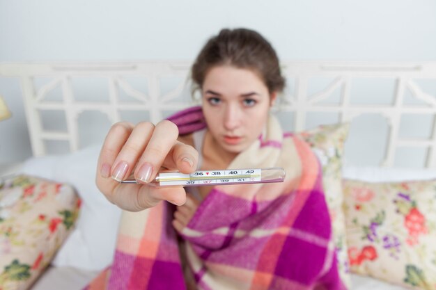 Jeune femme malade en couverture avec thermomètre