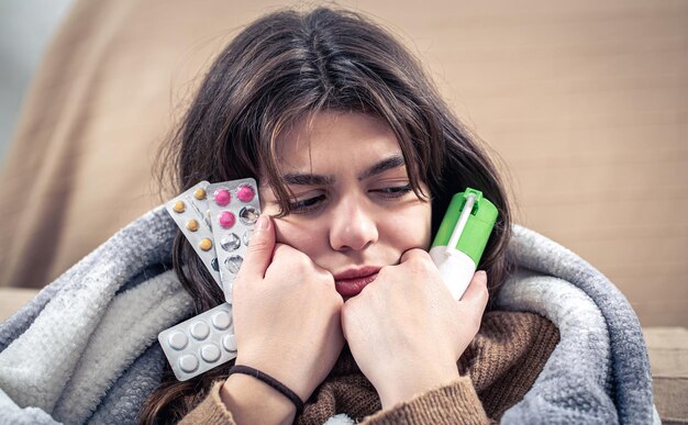 Une jeune femme malade tenant un spray contre la toux et des pilules dans ses mains