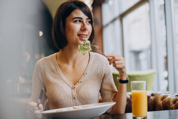Jeune femme mangeant un petit déjeuner sain avec du jus dans un café