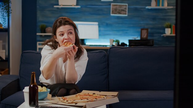 Jeune femme mangeant une tranche de pizza de fort et buvant de la bière