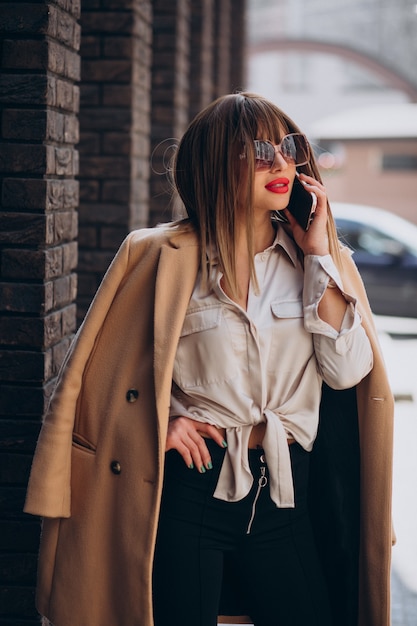Jeune femme en manteau beige à l'aide de téléphone dans la rue