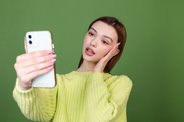 Jeune femme avec un maquillage naturel parfait, de grandes lèvres brunes sur un mur vert avec un téléphone portable, prendre un selfie en se photographiant