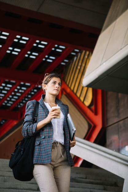 Jeune femme marchant sur l&#39;escalier, tenant une tablette numérique et café à emporter