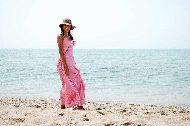 Jeune femme marchant le long de la plage avec robe rose