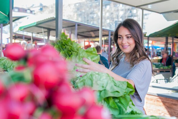 Jeune femme sur le marché. Bonne jeune fille en train de choisir des légumes. Portrait d'une belle jeune femme choisissant des légumes à feuilles vertes
