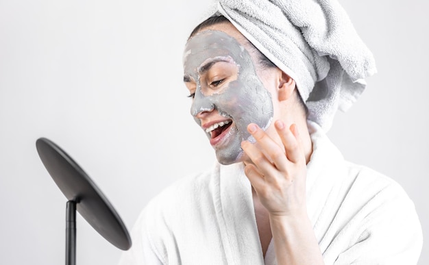 Jeune femme avec un masque d'argile sur son visage devant un miroir