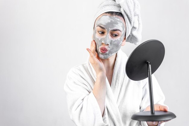 Jeune femme avec un masque d'argile sur son visage devant un miroir