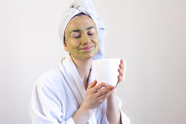 Jeune femme avec un masque de beauté vert sur son visage et avec une tasse