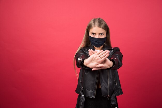 Jeune femme en masque médical debout et croisant les mains faisant signe négatif de refus