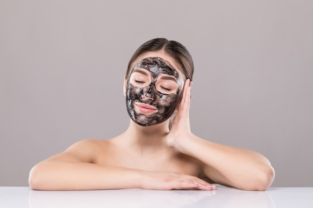 Jeune femme avec un masque noir purifiant sur son visage isolé sur mur blanc